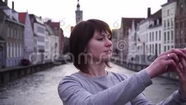女孩游客在比利时布鲁日日落时在智能手机上自拍。