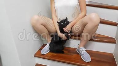 女孩正坐在房子的楼梯上，两腿之间抱着一只黑猫，抚摸着它