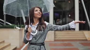 帅气的年轻女商人仰望天空，举起手来检查雨是否停了。她微笑着靠近