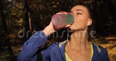 公园里的女跑步者。 女人喝着<strong>水站</strong>在秋天的公园里，满是落叶