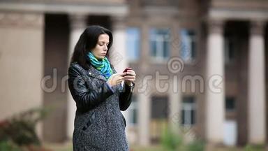 站在公园中央的迷人的年轻女子，用她的智能手机录音