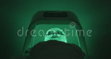 LED灯治疗年轻女子的脸与面具和眼镜躺在特殊的小屋在水疗沙龙。 变化
