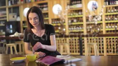 一个年轻的女孩喝咖啡，在咖啡馆或餐馆看时尚杂志，女人读杂志，喝酒