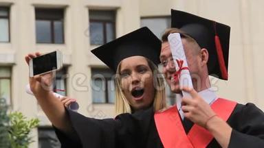 女<strong>毕业生</strong>和男<strong>毕业生</strong>穿着学术服装和帽子拍摄视频电话