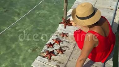 两帧视频。 穿着红色衣服的女人坐在码头上，认为是红星鱼。 红海星。 特写镜头。 A.