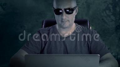 一个穿T恤和眼镜的年轻人坐在电脑前.. 一个男人在深夜在电脑上工作，