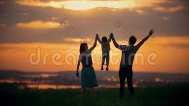 一家人牵着手爸爸妈妈在空中养育孩子，一家人玩得很开心，橙色的日落，夏天
