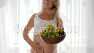 裸腹微笑的女人端着新鲜水果的盘子，看着镜头