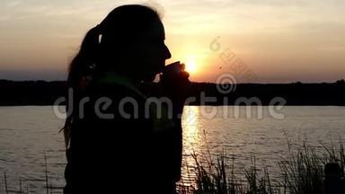漂亮的女人坐在湖畔喝热水瓶里的茶