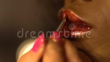 专业的化妆师正在使用非洲女人的<strong>大嘴唇</strong>上的画笔涂抹红色光泽的口红。 没有