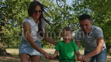 幸福的家庭，母亲，父亲和儿子都在大自然中行走，孩子在骑自行车，父母帮助他