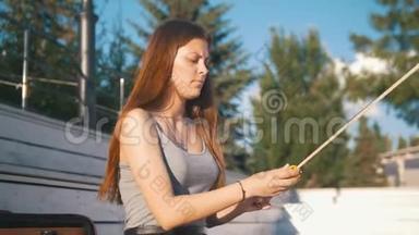 年轻女子小提琴手在公园的长凳上为小提琴擦弓