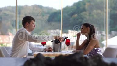在豪华餐厅约会的漂亮年轻夫妇。 那个优雅的人正在酒杯里倒红酒。