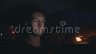 一个年轻人在夜间坐在马路上的车里用智能手机
