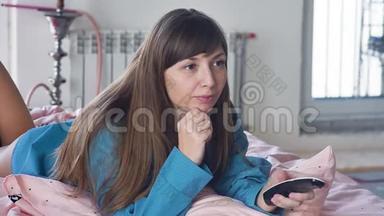 一个有魅力的女人在遥控器的帮助下选择一个<strong>电视频道</strong>。 躺在床上看电视的女人