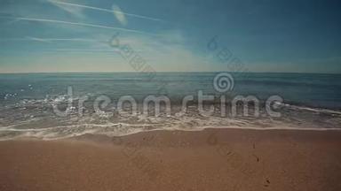 平静的大海，沙滩上有一些波浪破碎。 夏日的天空中有一些飞机的轨迹