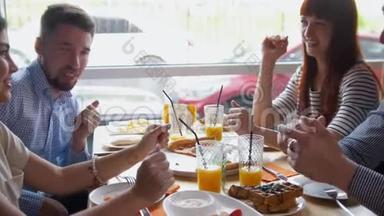 四个快乐的年轻朋友在咖啡馆里<strong>讲故事</strong>，吃早餐-披萨、果汁、甜点