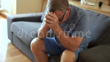 一位抑郁症老人坐在沙发上。 他低着头，看着养老金领取者的问题