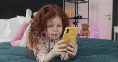 有趣的红头发<strong>小</strong>女孩与黄色智<strong>能手</strong>机躺在床上和使用智<strong>能手</strong>机。 沟通，播放，APP..