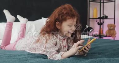 有趣的红头发小女孩与黄色智能<strong>手机躺</strong>在床上和使用智能<strong>手机</strong>。 沟通，播放，APP..