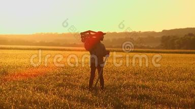 农夫拿着铲子和盒子在田里散步。 他们携带种植树木的设备。 在日落的时候。 侧视图