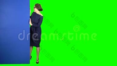 女商人从一块蓝色的木板后面往外看，露出了一个行头。 绿色屏幕