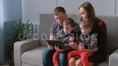 带平板电脑的家人。 妈妈，爸爸和两个儿子双胞胎坐在沙发上玩平板电脑游戏。