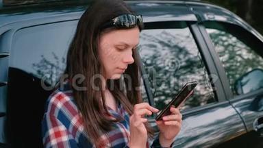 女人在站在车旁边的电话上<strong>发信息</strong>。
