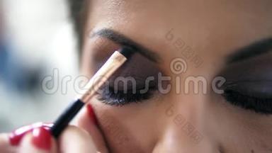 化妆师的特写镜头`他的手用画笔为一个有假睫毛的模特画眉毛。 慢镜头
