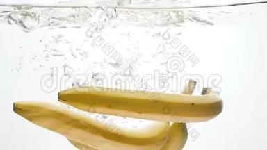 新鲜成熟的香蕉在白色背景下落入水中的慢镜头。 空气中的气泡漂浮