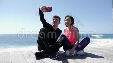 年轻的健康夫妇坐在海滩附近拿着电话，摆出自拍姿势。 快乐的<strong>男朋友</strong>和<strong>女友</strong>拍照