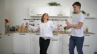 新婚夫妇在家穿着睡衣在厨房里快乐地跳舞，听<strong>音乐</strong>。 慢动作