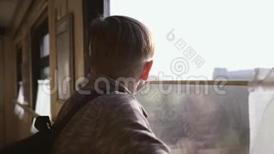 这个男孩站在火车窗口，看着窗外的风景。 坐火车旅行。 旅游业
