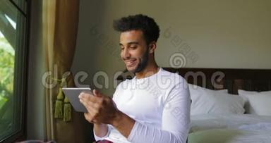 年轻的西班牙裔男子使用平板电脑快乐的微笑男人在网上聊天的大窗口与热带花园景观
