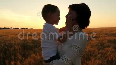 一位快乐的<strong>母亲</strong>把她的<strong>孩子抱</strong>在怀里，背景是日落时的麦田。 一个快乐的<strong>孩子</strong>亲吻