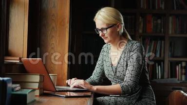戴眼镜的女商人在图书馆或豪华办公室里用笔记本电脑工作。 在后台，书架上放着书