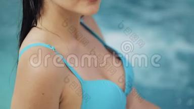 年轻女子穿着蓝色泳衣，在池中摆着绿松石水，特写镜头