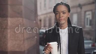 一幅严肃的非洲裔美国商人的肖像，穿着西装，在城市里<strong>走来走去</strong>，喝着咖啡。 她看<strong>上去</strong>
