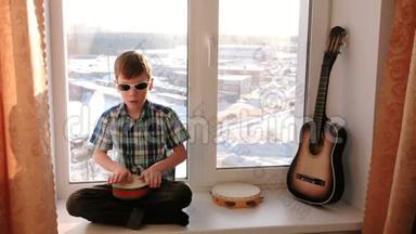演奏乐器。 男孩坐在窗台上打鼓。