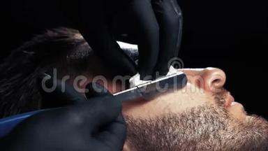 一个英俊的男人用剃刀在一家理发店的专业理发师那里刮胡子