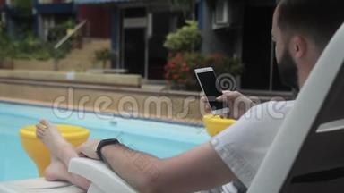 成年男子正在游泳池附近<strong>滚动</strong>他的智能手机<strong>屏幕</strong>。