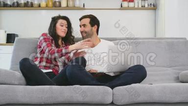 幸福的男人和幸福的男人在家里一起坐在沙发上，微笑着的年轻夫妇用电脑享受早晨的咖啡