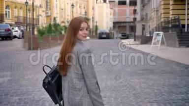 年轻的女人，留着长长的姜发，在城市里散步，回头看，拿着背包，城市街道背景，回来