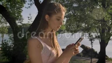 在河边公园，年轻漂亮的女人在手机上发短信，微笑着，美丽的景色