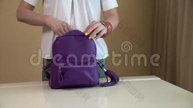 <strong>一个</strong>年轻的女人拿出她紫色背包里的<strong>东西</strong>，把所有的<strong>东西</strong>放在一张白色的桌子上。 女式手袋的内容