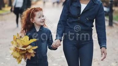 一位美丽的母亲和她可爱的小女儿在秋天的公园里散步。 他们在人群中间走来走去