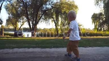 夏天在公园的小径上散步的金发小孩子。 孩子夏天去吃青草。 快乐男孩