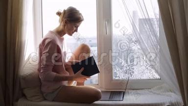 漂亮的年轻女人，坐在窗台上的记事本。 外面冬天