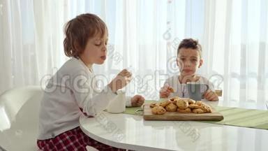 两个男孩在现代厨房吃<strong>早餐</strong>。 男孩吃带牛奶的饼干。 厨房里的白色<strong>桌子</strong>。 母亲和两个儿子