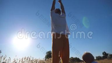小孩子坐在草地上，看着爸爸在阳光明媚的日子里练习瑜伽。 年轻的父亲